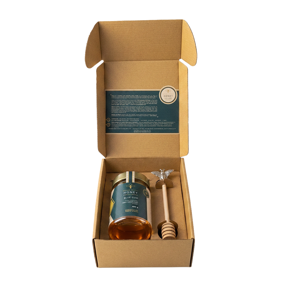 An open gift box holding a jar of Meant To Bee Blue Gum honey alongside a wooden honey dipper.