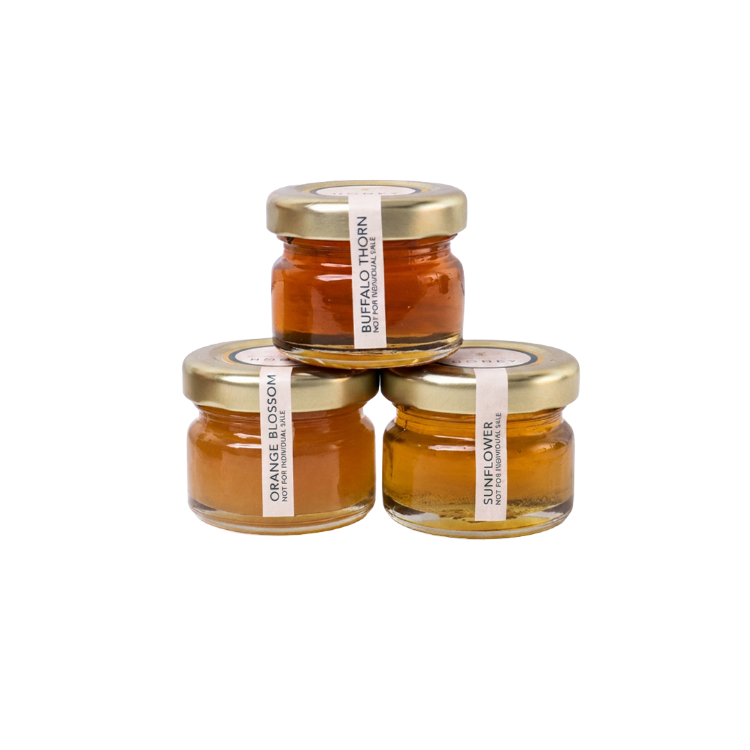 Three mini jars of Meant To Bee honey grouped together, labelled Buffalo Thorn, Orange Blossom, and Sunflower.